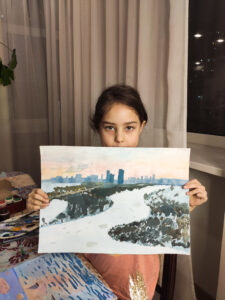 Девочка держит свою картину, на которой изображено Строгино